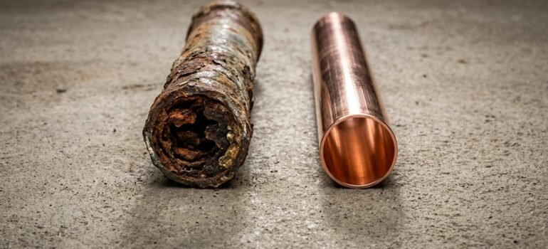 Side-by-side comparison of a corroded galvanized steel water pipe and a new clean copper pipe, showing why older Ogden homes need repiping.