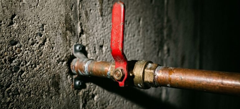 Main water shut-off valve with red lever handle on a copper supply line — the first thing to know in a plumbing emergency.